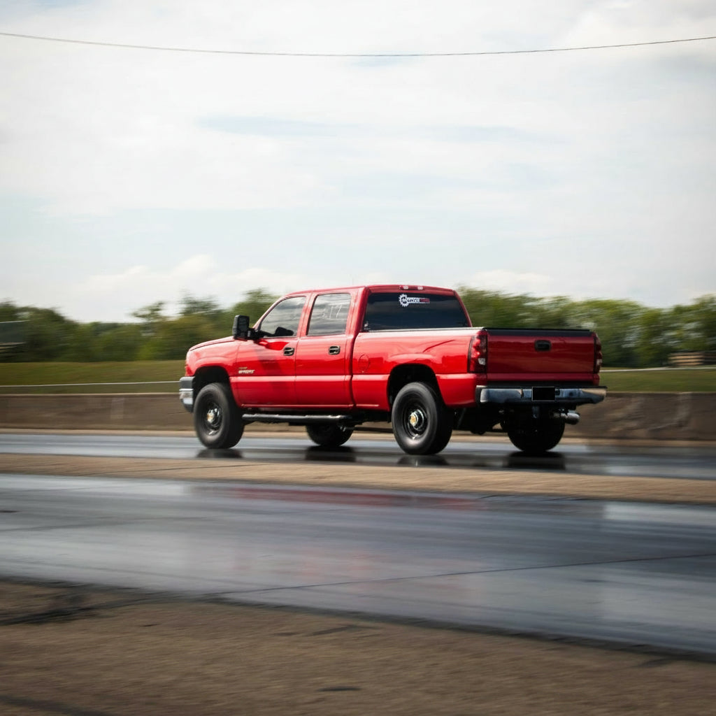 A red pickup truck driving on a wet road under a blue sky with white clouds.